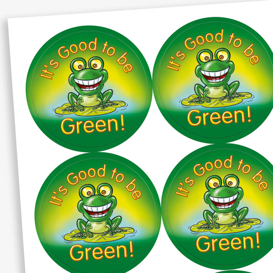 Circular stickers with a green background central is a cheerful green frog illustration with wide eyes and a big smile, sitting on a lily pad.  The phrase 'IT'S GOOD TO BE GREEN' in bold yellow lettering surrounds the frog