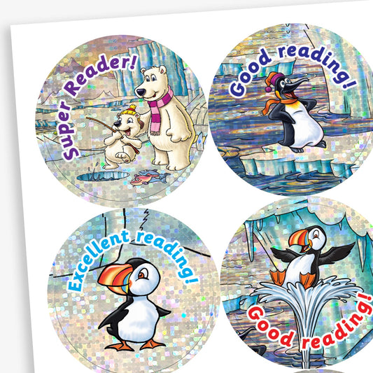 Snapshot of a sheet of holographic circular reading reward stickers for children with a shiny, icy background. Top left: a polar bear and cub reading together with the phrase 'Super Reader!'. Top right: a penguin wearing a hat and scarf with the text 'Good reading!'. Bottom left: a puffin standing proudly with 'Excellent reading!'. Bottom right: a puffin jumping out of water with the words 'Good reading!'.