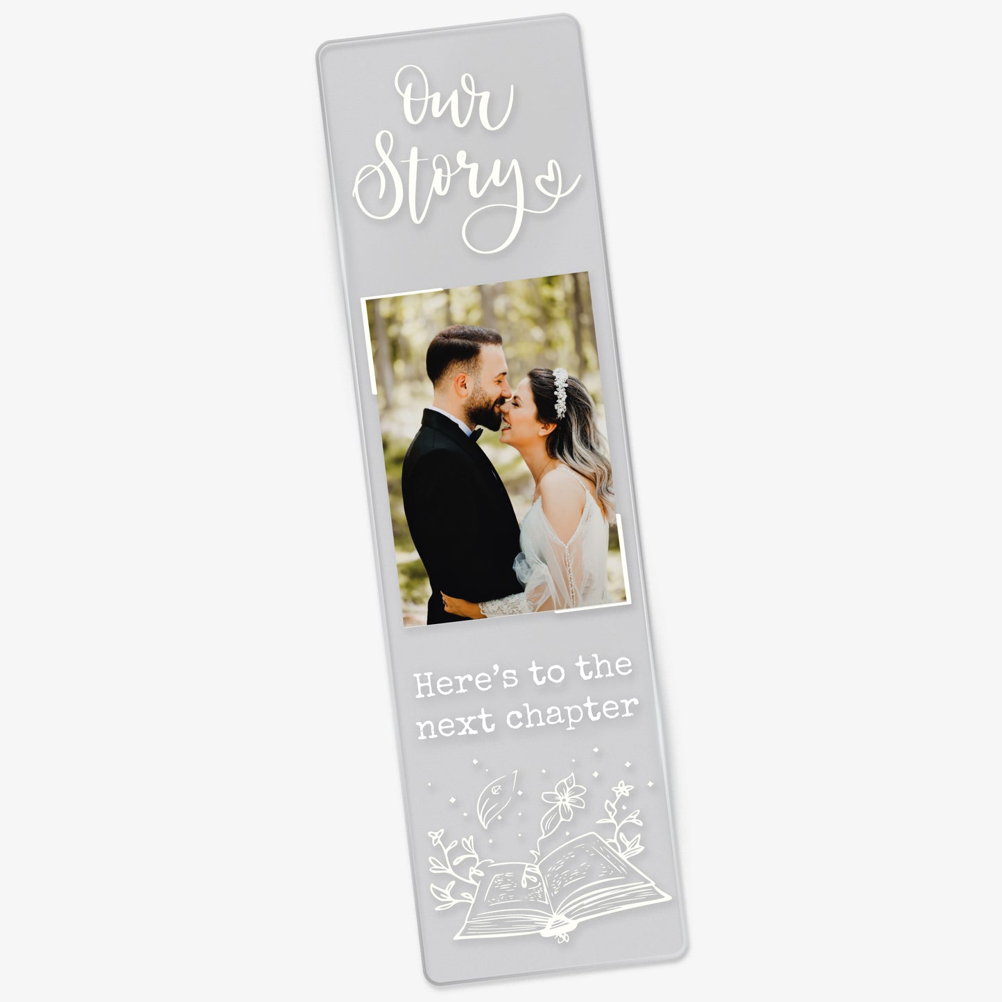 Clear acrylic wedding-themed bookmark featuring the phrase 'Our Story' at the top, a photo of a couple in wedding attire, and the words 'Here’s to the next chapter' in white font above an illustrated open book with magical elements.