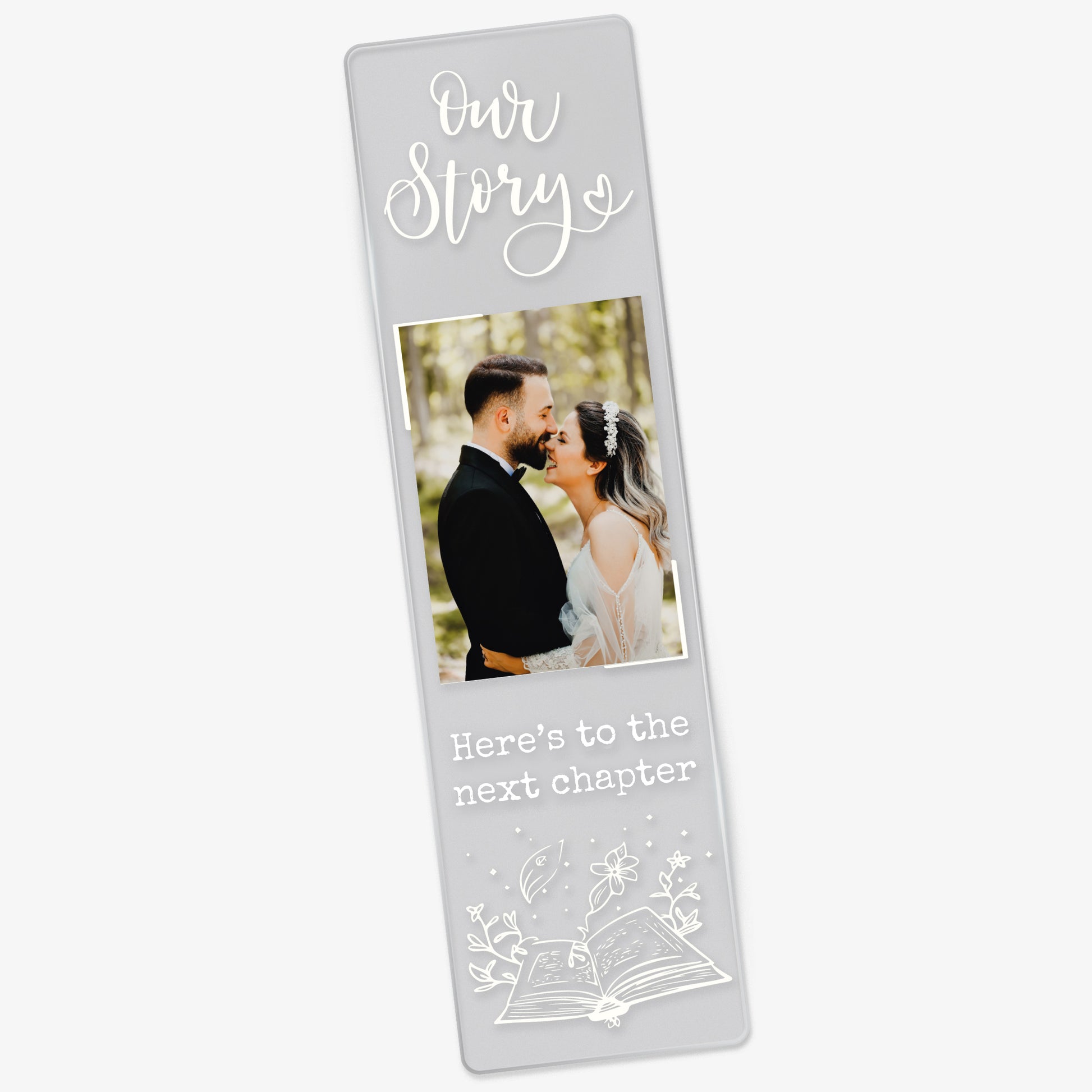 Clear acrylic wedding-themed bookmark featuring the phrase 'Our Story' at the top, a photo of a couple in wedding attire, and the words 'Here’s to the next chapter' in white font above an illustrated open book with magical elements.