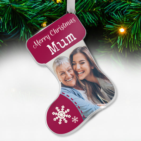 Stocking-shaped acrylic Christmas tree ornament with a maroon design, white snowflake decorations, and the message 'Merry Christmas Mum' at the top, featuring a photo of two smiling women, one older and one younger, hugging each other, hanging on a tree with fairy lights.