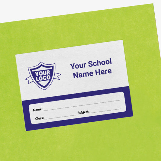 Green exercise book with a customisable white and navy label on the front. The label includes a placeholder shield icon reading 'Your Logo' and text stating 'Your School Name Here'. Below are blank lines labelled 'Name', 'Class', and 'Subject' for personalisation.