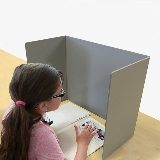 A grey, plastic coated board stood in front of a child doing a test to give privacy.
