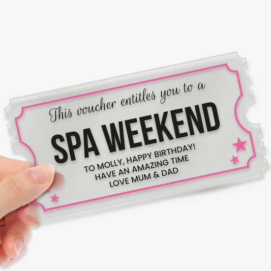 A hand holding a rectangular acrylic voucher shaped like a ticket, with decorative notched edges. The design features pink borders and stars. The text reads: 'This voucher entitles you to a SPA WEEKEND. To Molly, Happy Birthday! Have an amazing time. Love Mum & Dad'. The overall style is elegant and celebratory, suitable as a personalised gift.