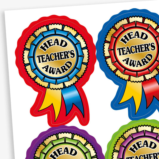 A sheet of brightly coloured stickers shaped like award rosettes with the text 'Head Teacher's Award' in bold black letters on a gold centre. Each rosette has a different colour combination, including red, blue, purple, and green borders, with matching ribbon tails