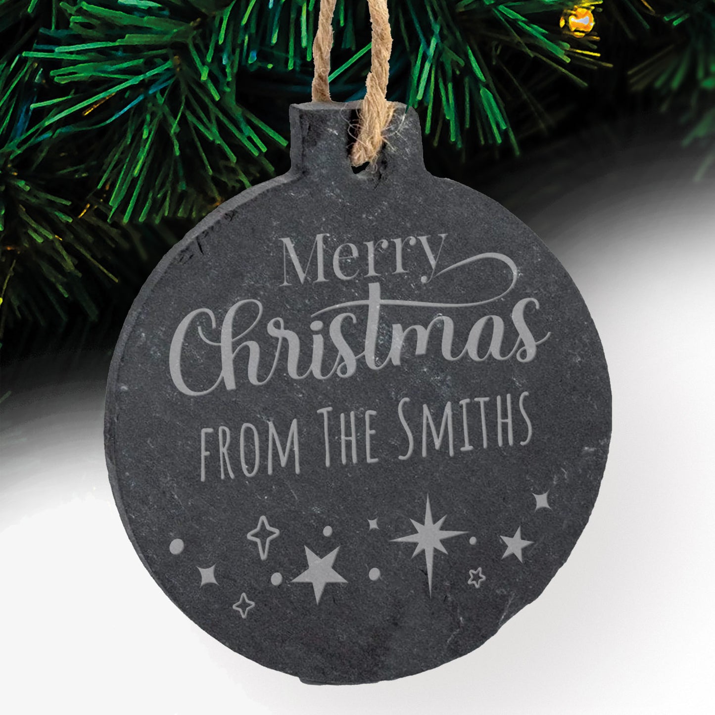 Round slate Christmas bauble with 'Merry Christmas from The Smiths' text and star designs, hanging against a Christmas tree background.