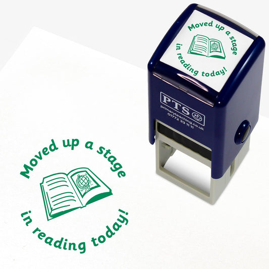 A 25mm round pre-inked teacher stamper with green ink, featuring a central design of an open book with lines on the left page and a picture of a globe on the right page.  Above the image is the wording 'Moved up a stage' and underneath the words 'in reading today!'.