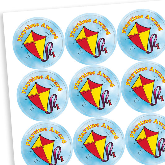 A sheet of circular reward stickers with the phrase 'Playtime Award' in orange text. Each sticker features a red and yellow kite with a purple ribbon tail flying against a soft blue sky background, symbolising positive behaviour during playtime.
