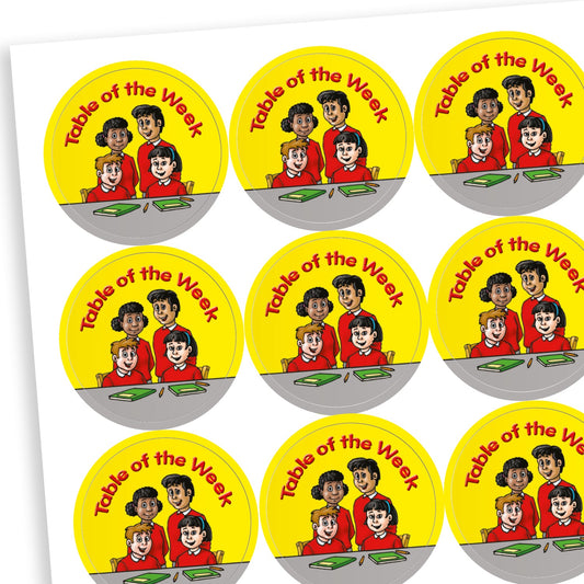 A sheet of circular reward stickers with a yellow background and the phrase 'Table of the Week' in red text. Each sticker features an illustration of four smiling children sitting together at a table with books and pencils, representing teamwork and good classroom behaviour.