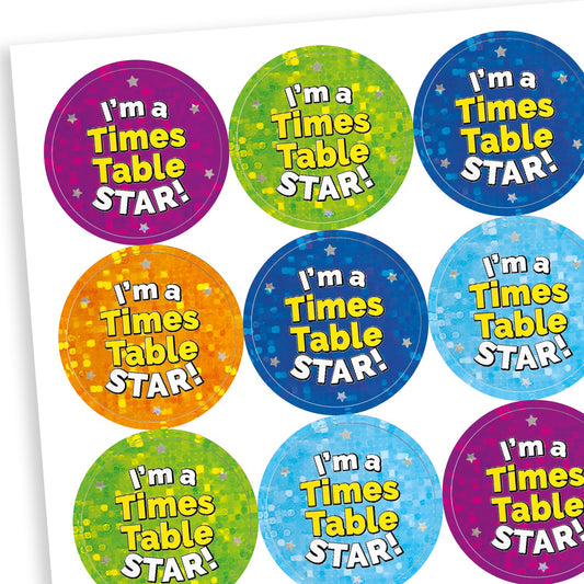 A sheet of round holographic reward stickers with the phrase 'I'm a Times Table STAR!' in bold white and yellow text. The stickers have starry backgrounds in various bright colours including blue, red, green, purple, and turquoise, creating a cheerful and encouraging appearance.