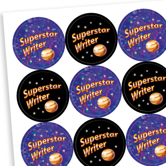 A sheet of circular, holographic reward stickers with the phrase 'Superstar Writer' in bright text. Each sticker features a planet illustration and a starry background. Half the stickers have a black background with orange and white text, while the other half have a sparkly purple background with blue and orange text, creating a cosmic theme.