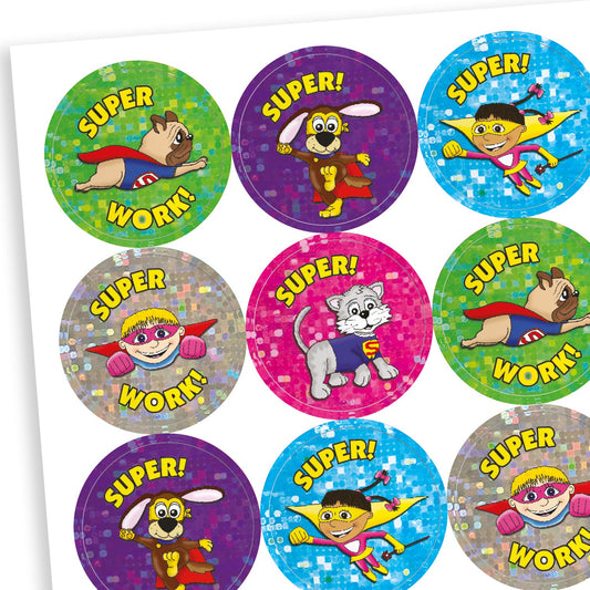 A sheet of circular, holographic, reward stickers with the phrase 'SUPER WORK!' in bold yellow text. Each sticker features a different cartoon superhero character, including a flying dog, bunny, cat, girl, and boy in colourful costumes. The backgrounds are sparkly and brightly coloured in shades like green, purple, blue, pink, and silver.