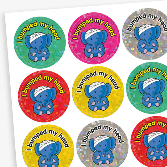 Holographic circular stickers with colourful backgrounds, central is a blue elephant with a bandage on their head.  The phrase 'I bumped my head' in bold lettering is above the elephant.
