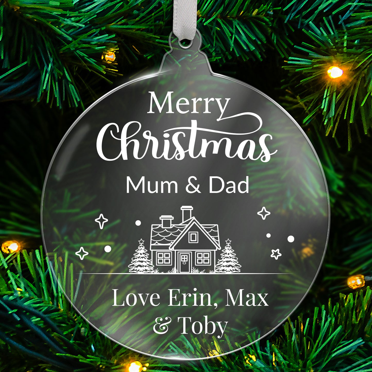 Round clear acrylic Christmas tree ornament with white design reading 'Merry Christmas Mum & Dad', featuring a house with trees, stars, and snowflake details, with bottom customisable text 'Love Erin, Max & Toby' hanging on a green tree with fairy lights.