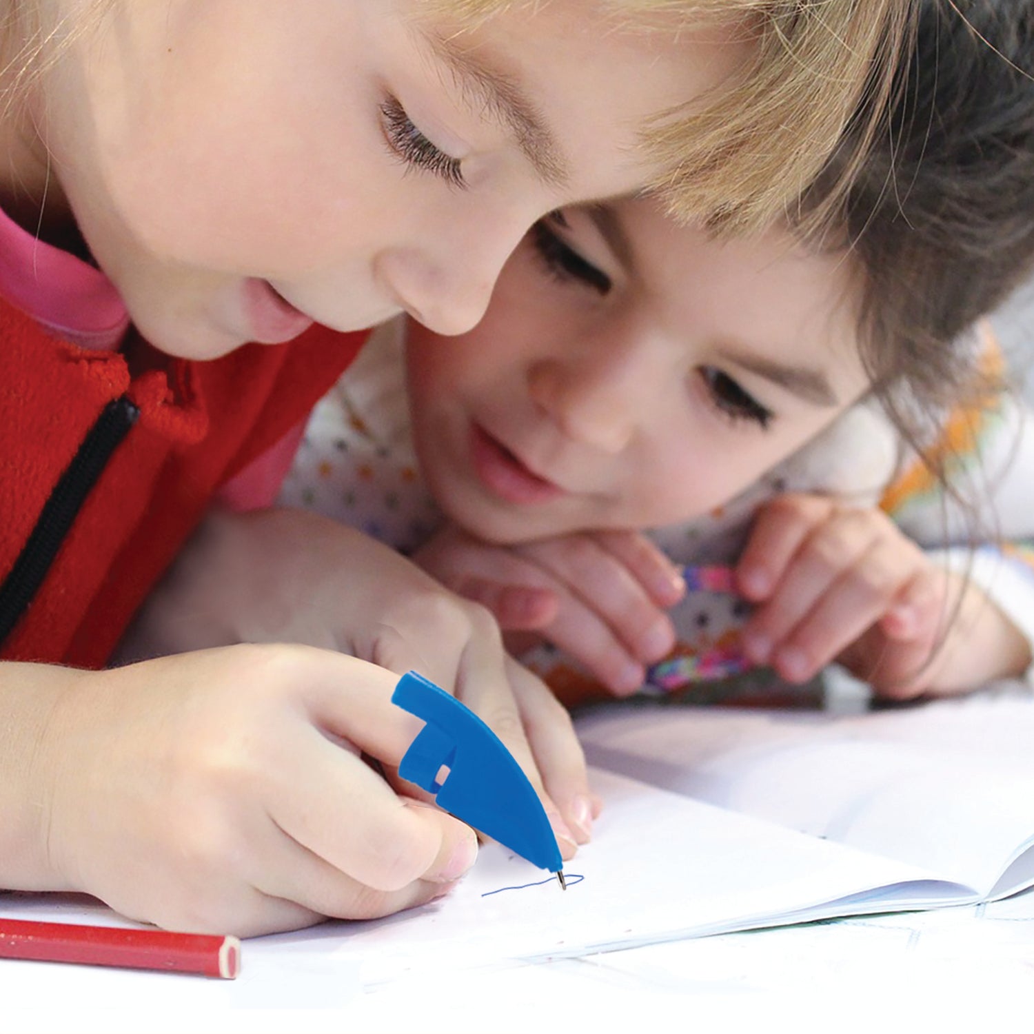 A photo of 2 girls using a pen on their fingertip and drawing in a book.