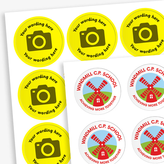 A sheet of circular stickers with a yellow background and the centre has a camera icon to indicate customisation.  Placeholder text 'Your wording here' arcs above and below the icon.  In front is an example image with a windmill logo uploaded and the text saying 'WINDMILL C.P. SCHOOL' above the logo and 'ACHIEVING MORE TOGETHER' below.