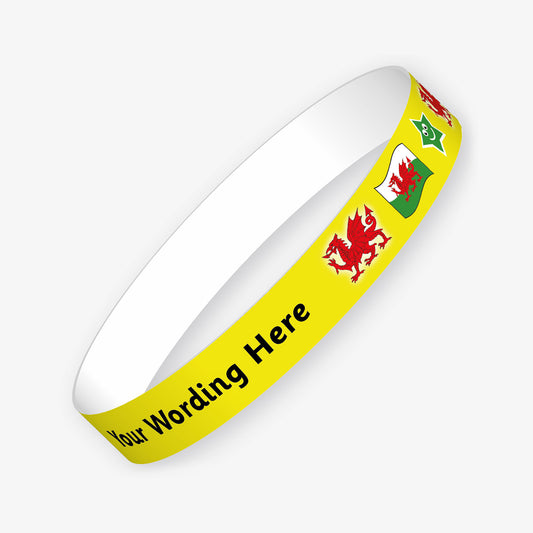 A customisable wristband with a yellow background and black text.  The centre is displaying the placeholder text 'YOUR WORDING HERE'.  Welsh images such as the flag and red dragon decorate the remaining wristband.