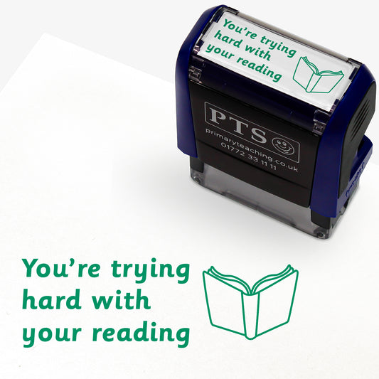 A rectangular self-inking stamper with a dark blue casing, displaying the green text 'You're trying hard with your reading' alongside an open book icon; the stamped impression measures 38mm by 15mm