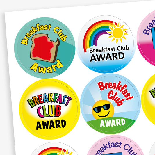 A sheet of colourful circular stickers with the text 'Breakfast Club Award'. Each sticker features different designs, including a toast with jam, a rainbow with the sun, stylised text, and a smiling emoji with sunglasses. The background colours include teal, blue, yellow, pink, and green.