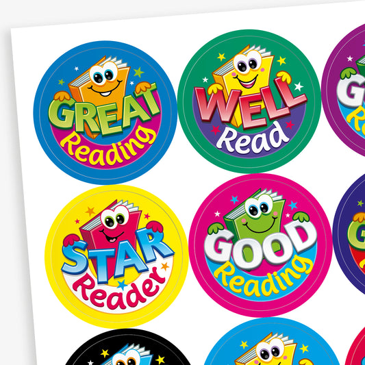 Sheet of colourful round reading reward stickers featuring cartoon book characters with smiling faces. Phrases include 'Great Reading', 'Well Read', 'Star Reader', and 'Good Reading', each in bold, playful fonts on vibrant backgrounds such as blue, green, yellow, and pink.