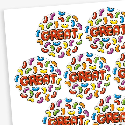 A sheet of jellybean scented round reward stickers, each featuring the word 'GREAT' in bold red-orange letters at the centre. The background is filled with a colourful pattern of jelly bean shapes in various colours including blue, yellow, green, purple, red, and orange. The playful design is vibrant and engaging,