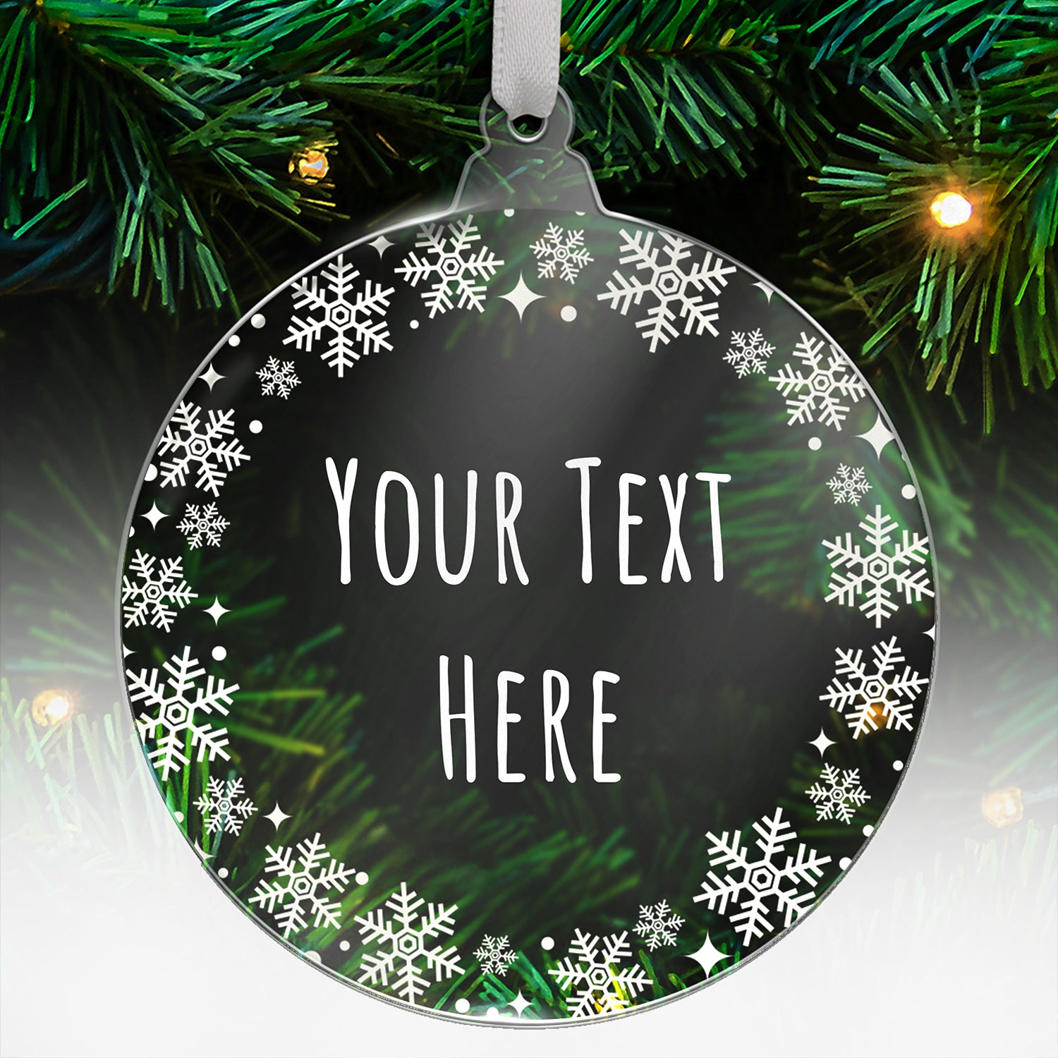 Round acrylic Christmas tree ornament with a dark background and decorative white snowflakes around the border, featuring the words 'Your Text Here' in a tall, narrow font, hanging on a tree with green branches and fairy lights.