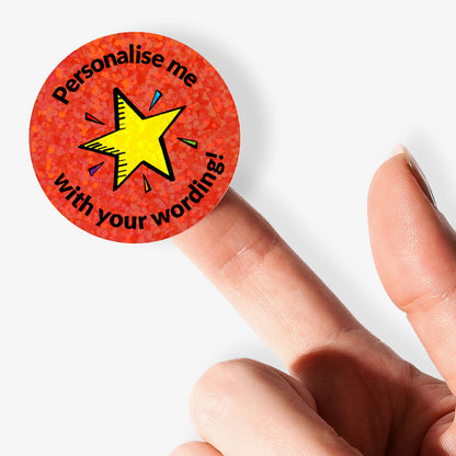 Personalised holographic round red sticker with yellow star and text 'Personalise me with your wording!' held by a finger.