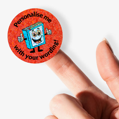 Personalised holographic round sticker with cartoon book character and text 'Personalise me with your wording!' held by a finger.