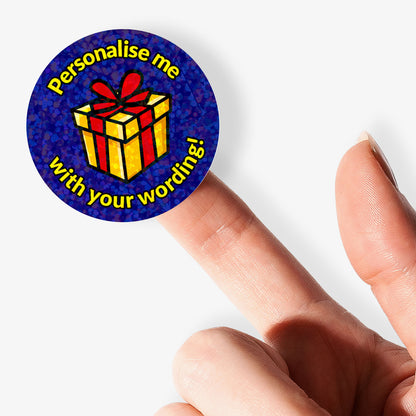 Personalised holographic round sticker with gift box design and text 'Personalise me with your wording!' held with finger.