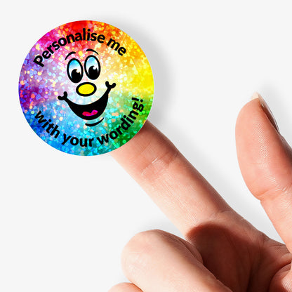 Colorful round sticker with a smiley face and text 'Personalise me with your wording!' held by a finger.