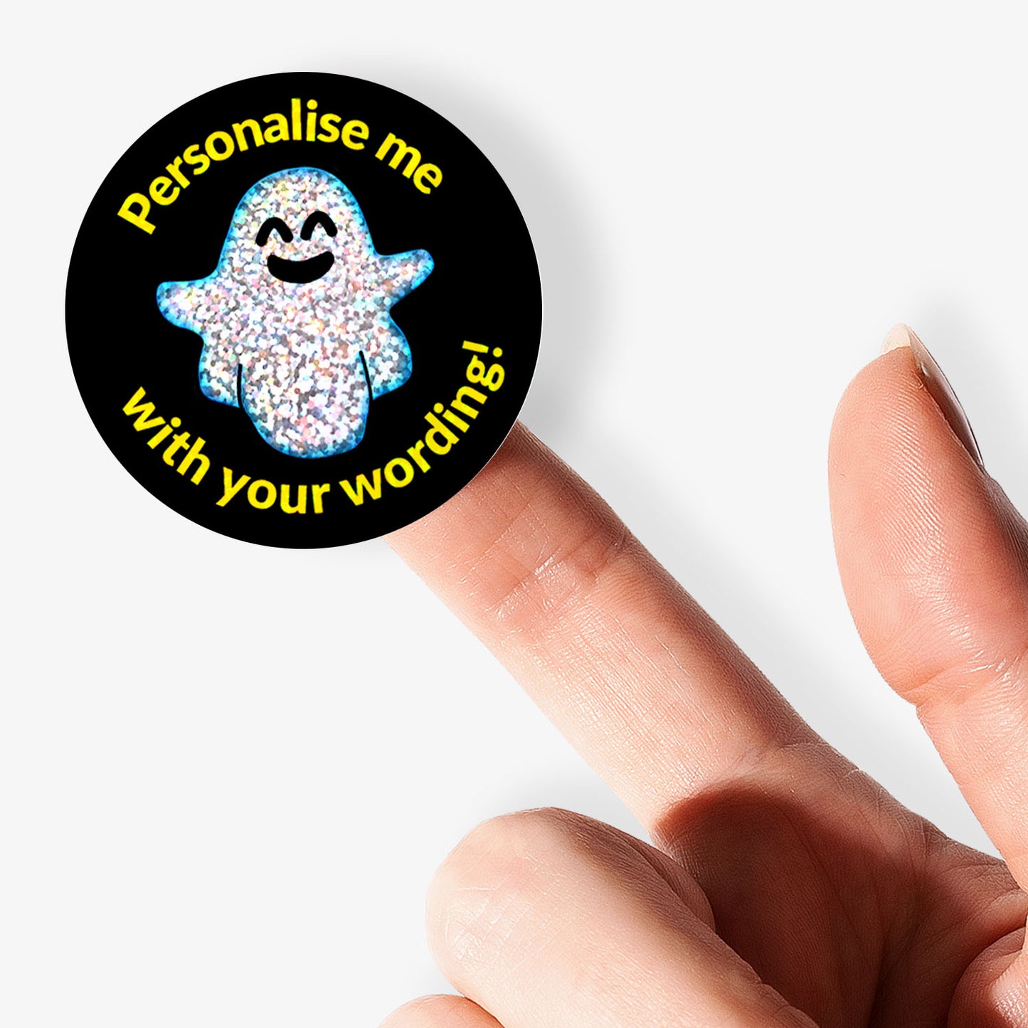 Circular sticker with sparkly spooky ghost design and personalised text held by hand.