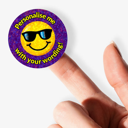 Smiley face with sunglasses stickers with 'Personalise me with your wording!' text, held by a hand.