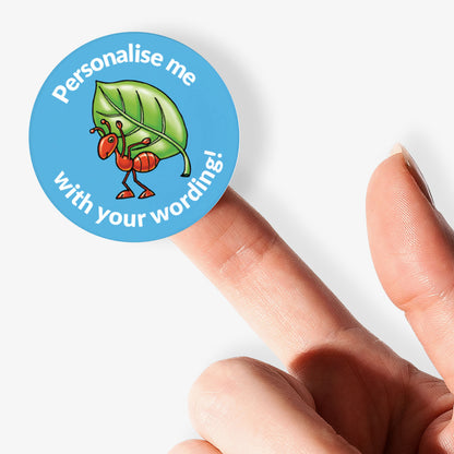 Sticker with a red ant and green leaf design, held by a finger on a white background.