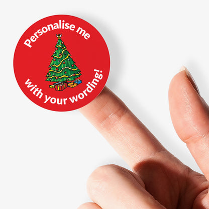 Round red sticker with Christmas tree and text 'Personalise me with your wording!' held by a finger.