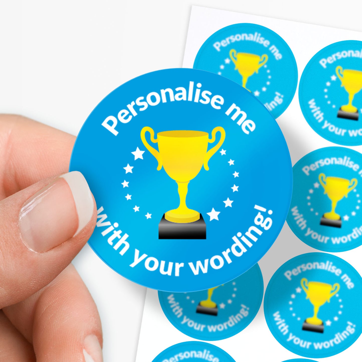 Round blue sticker with yellow trophy graphic and text 'Personalise me with your wording!' held by a hand.