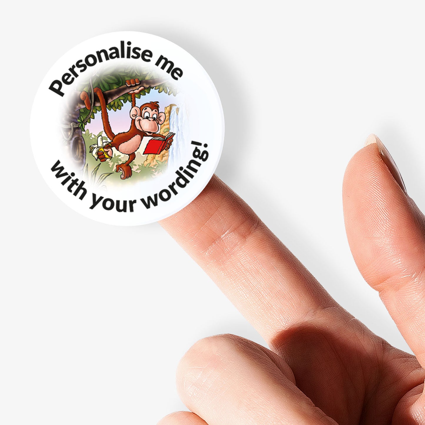 Circular sticker with cartoon monkey holding a book, text 'Personalise me with your wording', held between fingers on a white background.