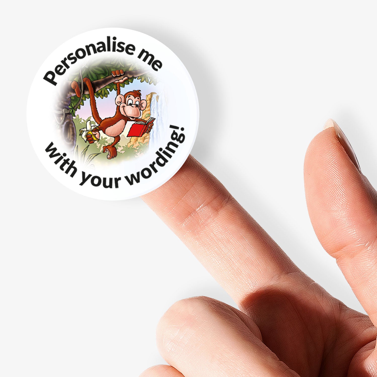 Circular sticker with cartoon monkey holding a book, text 'Personalise me with your wording', held between fingers on a white background.