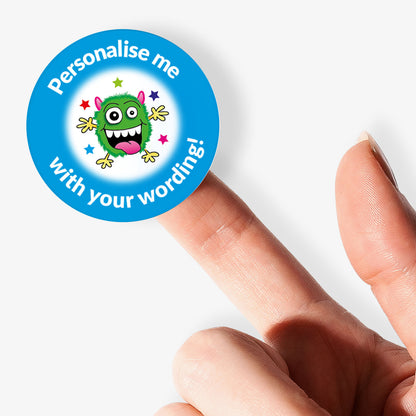 Circular sticker with a monster graphic and text 'Personalise me with your wording!' held between fingers.