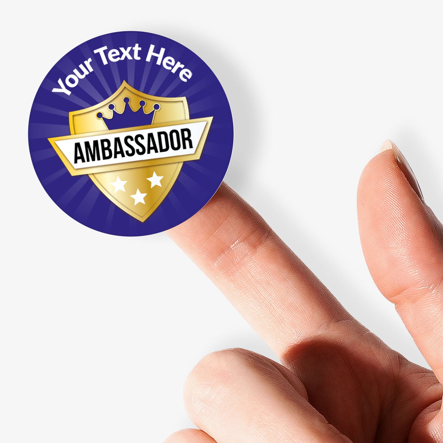 Round 'Ambassador' sticker with customizable text held between fingers on a white background