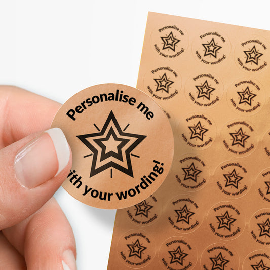 Round bronze label with star design and text 'Personalise me with your wording!' held by a hand, with a sheet of similar labels in the background.