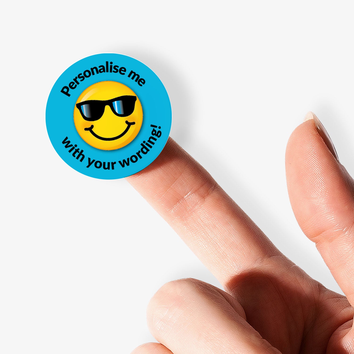 Round sticker with a smiley face wearing sunglasses and text 'Personalise me with your words!' on a blue background. Held by a finger