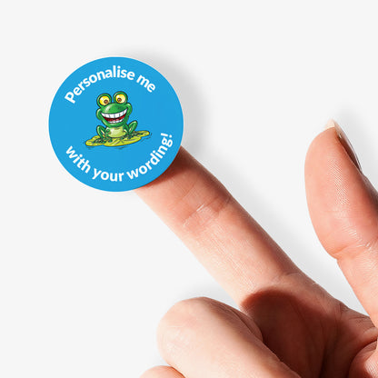 Round blue sticker with a frog graphic and text on a finger against a white background