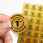 Sheet of circular stickers with 1st  in the middle and text on a gold background. Single sticker held between thumb and finger