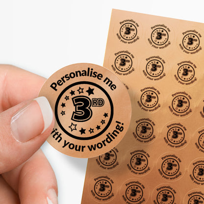 Sheet of circular stickers with 3rd in the middle and text on a bronze background. Single sticker held between thumb and finger