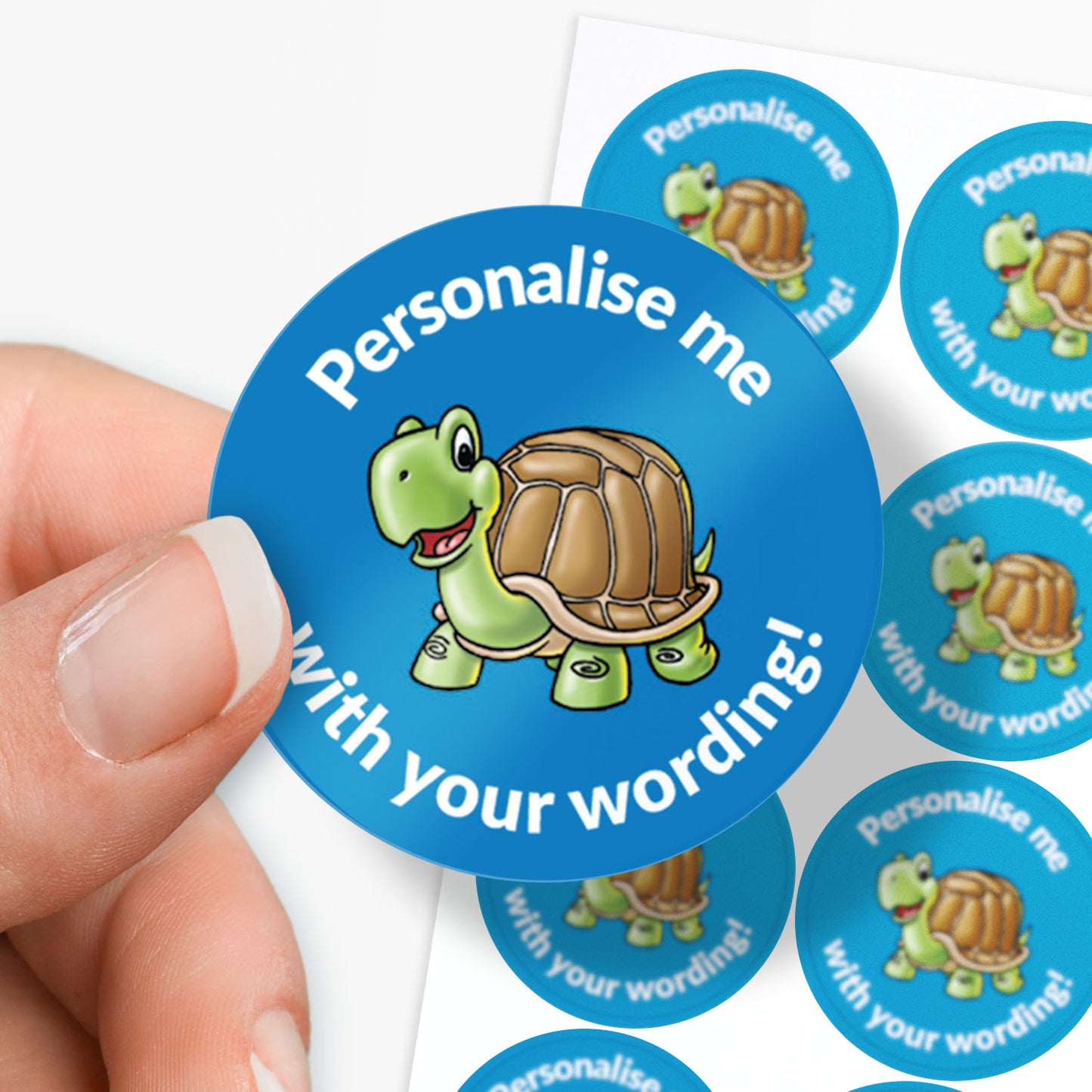 Round blue sticker with a turtle graphic and text 'Personalise me with your wording!' held by a hand.