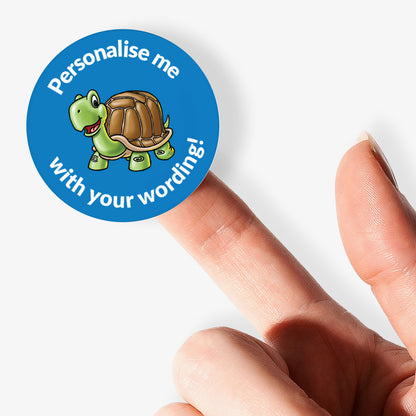 Sticker with a turtle design and text 'Personalise me with your wording!' held by a finger on a white background.
