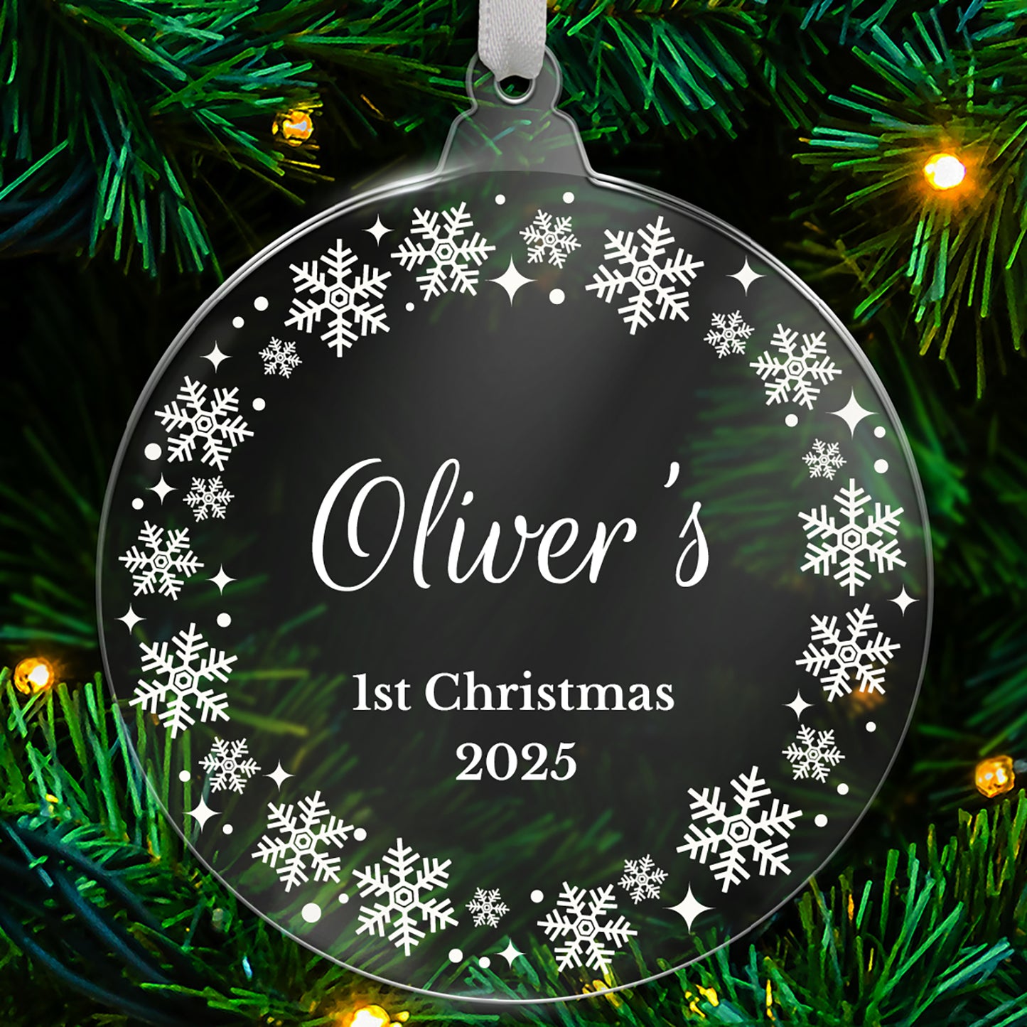 Decorative ornament with 'Oliver's 1st Christmas 2025' text on a black background with snowflakes, hanging on a Christmas tree.