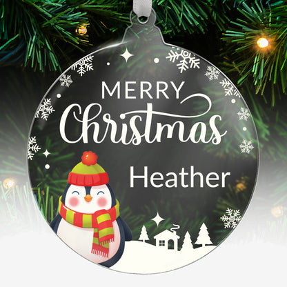 Round acrylic Christmas tree ornament featuring a festive penguin wearing a hat and scarf, with the message 'Merry Christmas' in white and space for custom text below, hanging on a tree with green needles and lights.