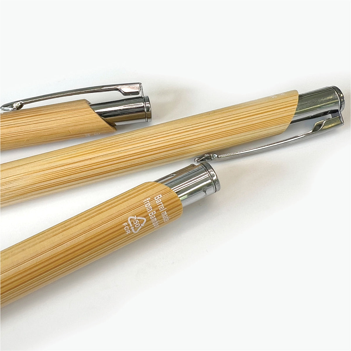 Close-up of several bamboo ballpoint pens, highlighting the natural wood-grain finish, metal clips and recycled material marking.