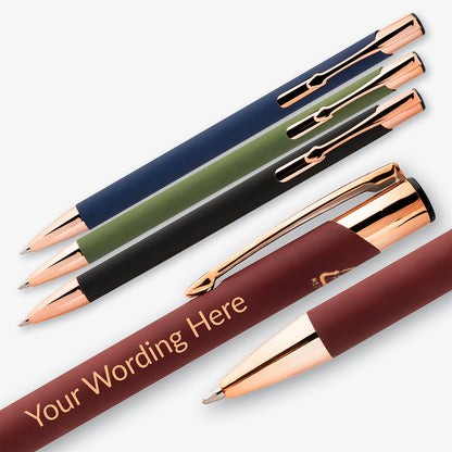 Black, green, navy and burgundy personalised pens with rose gold detailing arranged diagonally on a white background.